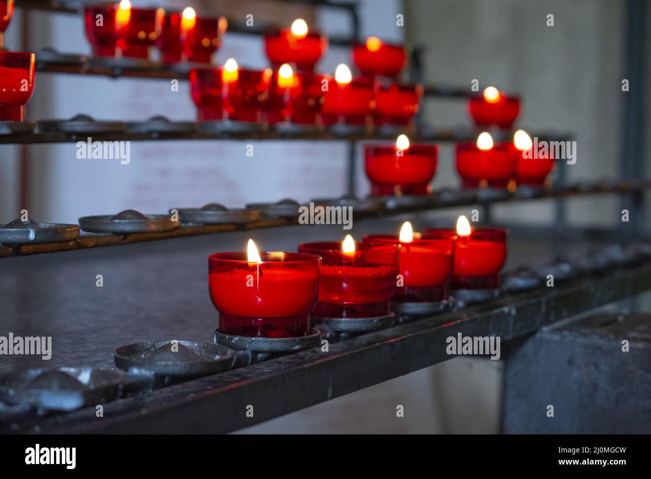 Burning red prayer candles inside a catholic church on a candle rack