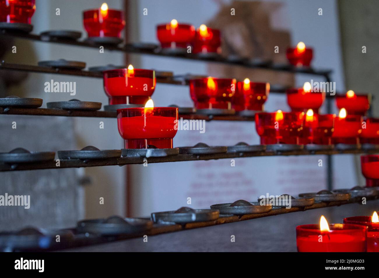 Burning red prayer candles inside a catholic church on a candle rack