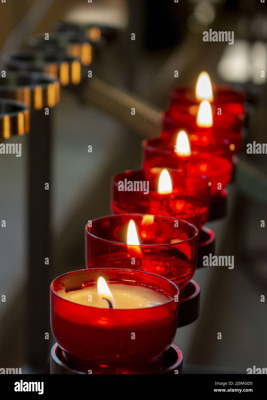 Burning red prayer candles inside a catholic church on a candle rack. Selective focus Stock