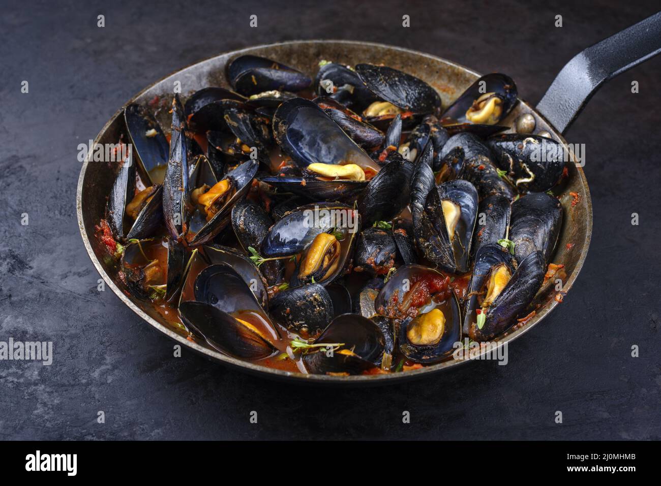 Traditional barbecue Italian blue mussel in tomato red wine sauce with herb and garlic as close-up in a rustic iron pan Stock Photo