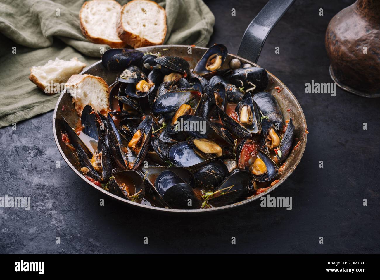 Traditional barbecue Italian blue mussel in tomato red wine sauce with baguette bread as close-up in a rustic iron pan Stock Photo