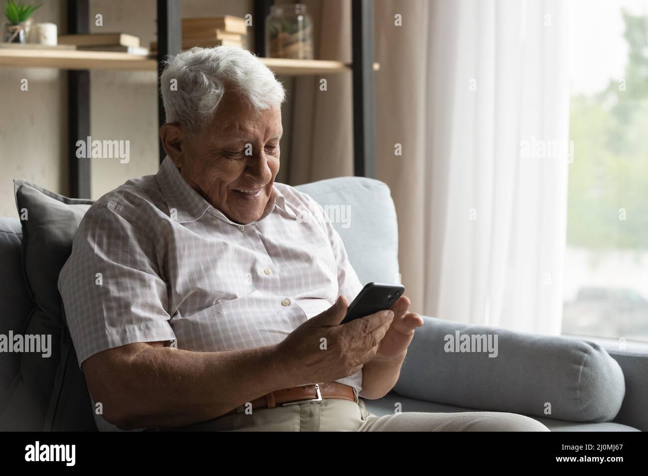 Smiling older grey-haired man using smartphone at home Stock Photo