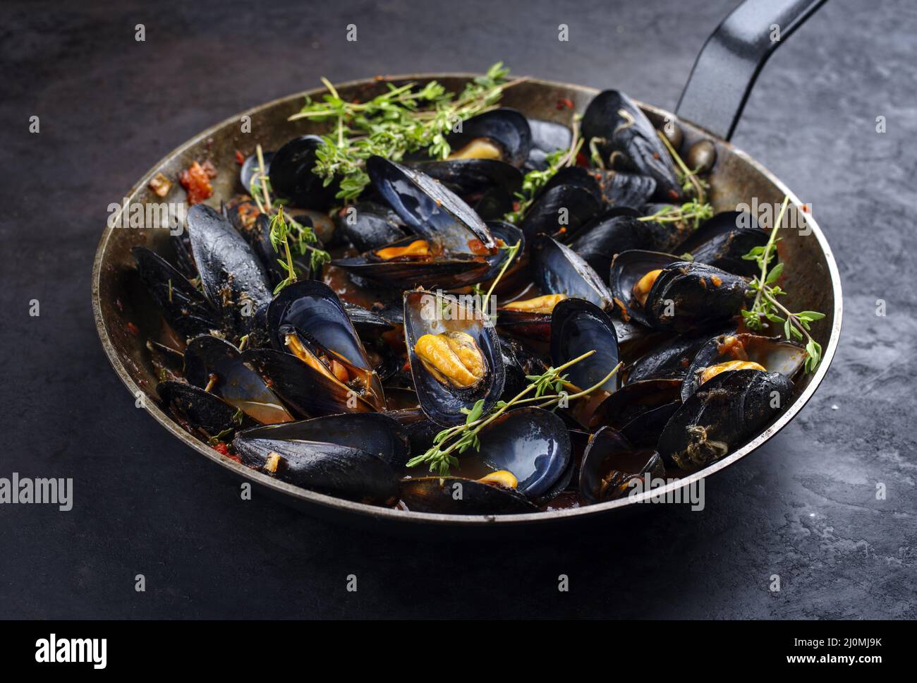 Traditional barbecue Italian blue mussel in tomato red wine sauce with herb and garlic as close-up in a rustic iron pan Stock Photo