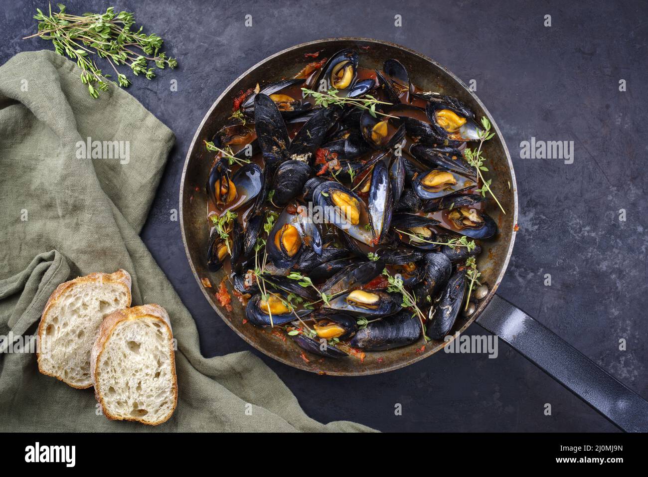 Traditional barbecue Italian blue mussel in tomato red wine sauce with baguette bread as top view in a rustic iron pan Stock Photo