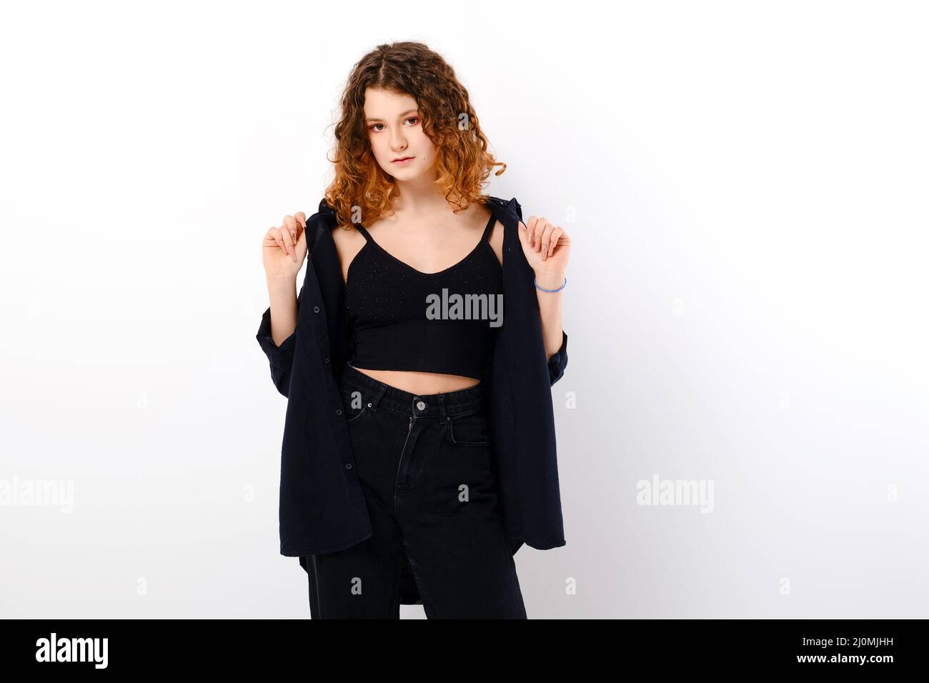 Serene caucasian teenage girl in casual clothing with colored ends of hair holds edges of black shirt over white studio background Stock Photo