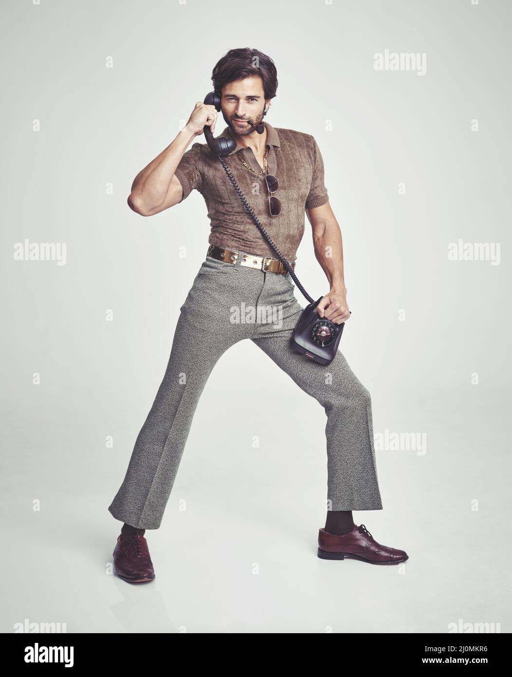 Doing everything with flair. A handsome man on a retro telephone while striking a pose. Stock Photo
