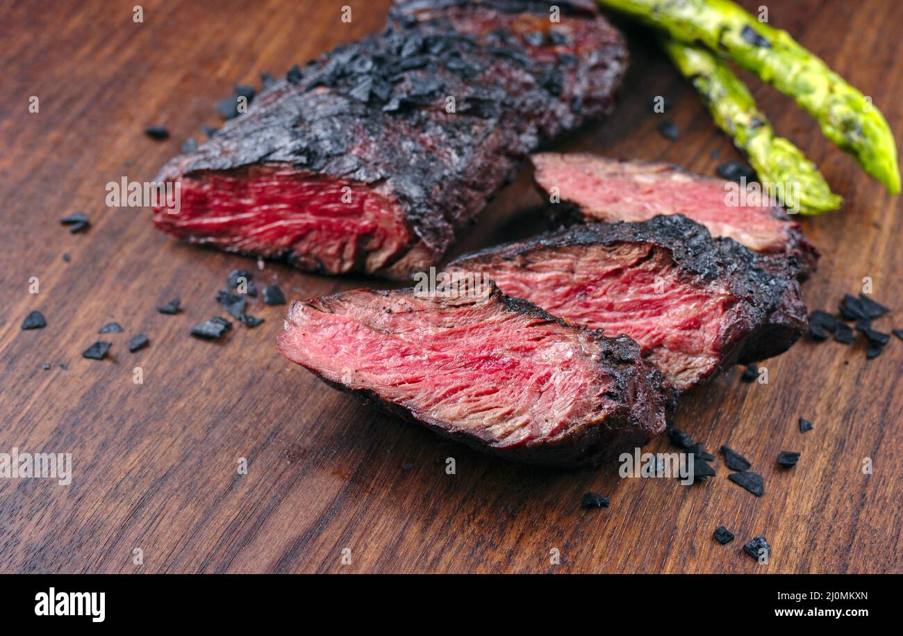 Modern style traditional barbecue wagyu onglet steak with green asparagus and black salt served as close-up on a wooden design b Stock Photo