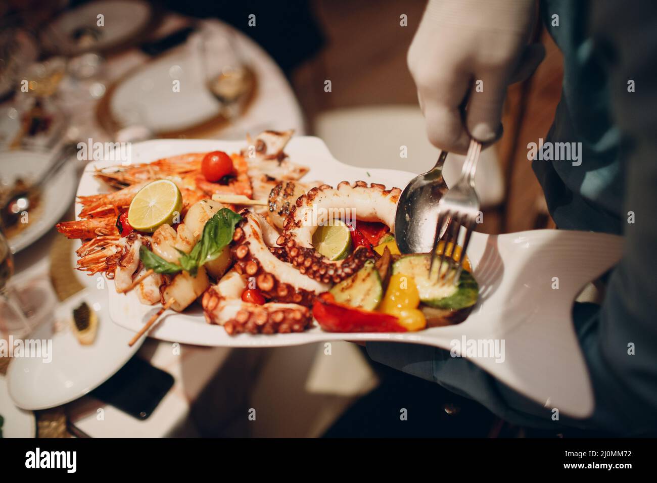 A waiter in a restaurant holds seafood dishes and serves a table catering Concept Healthy food octopus and crabs shellfish Stock Photo