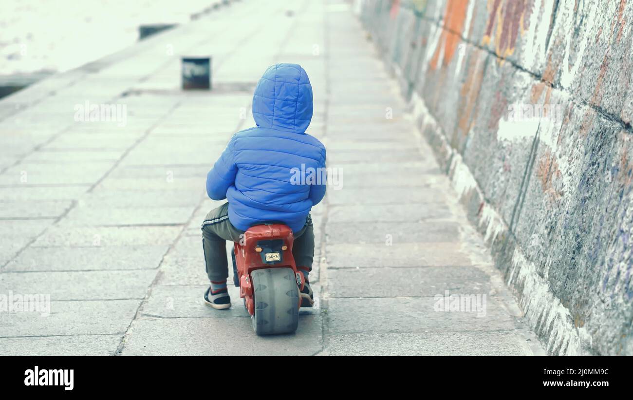 Boy in blue jaÑket ride balance bike near the river. Parents and children cocnception .City views. Weekend in the city. 26 of A Stock Photo