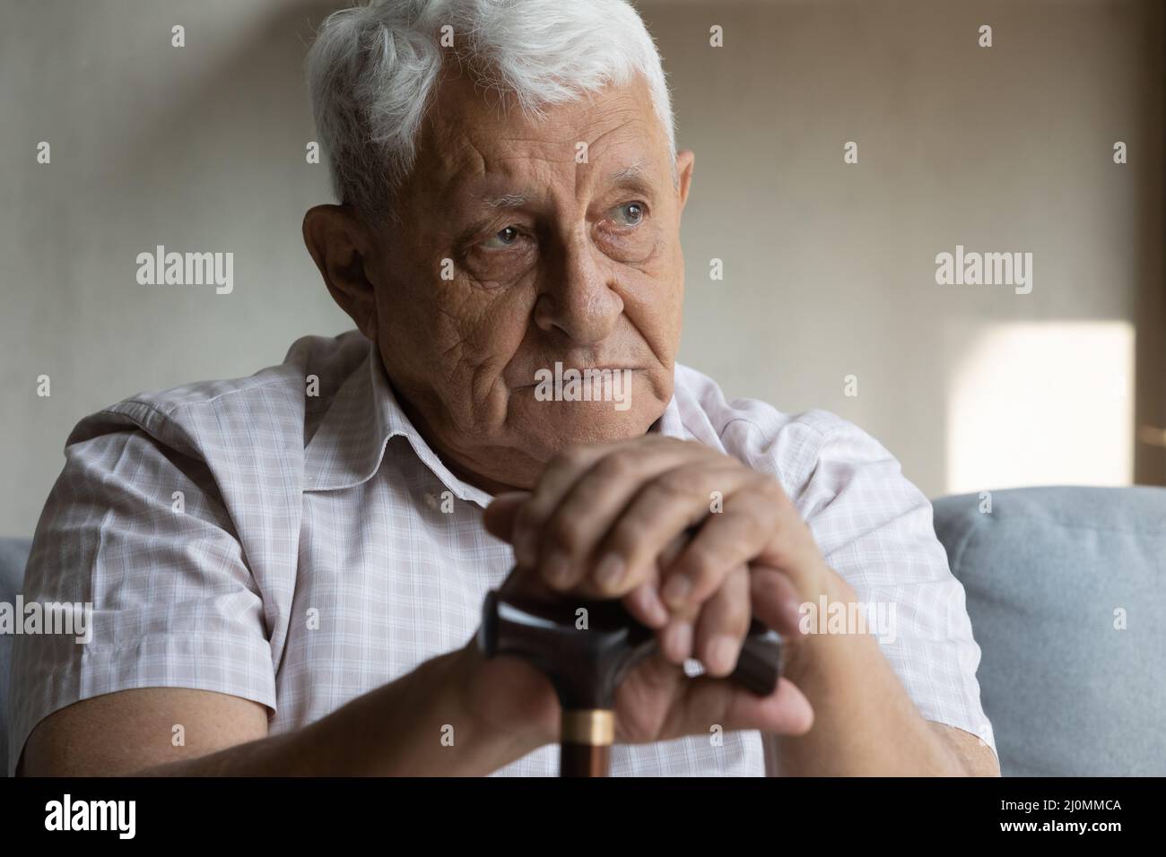 Older disabled man resting on couch hold cane looking upset Stock Photo