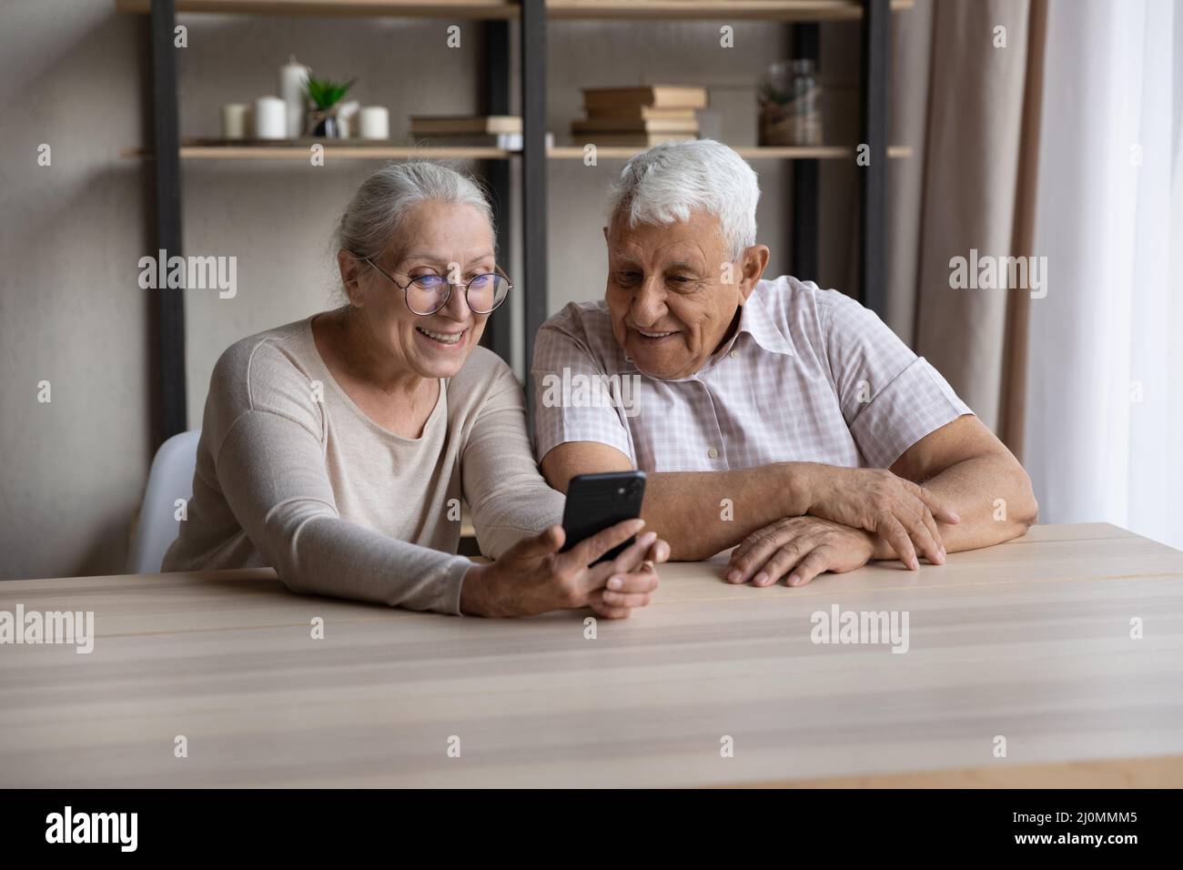 Smiling older couple sit at table using modern smartphone Stock Photo