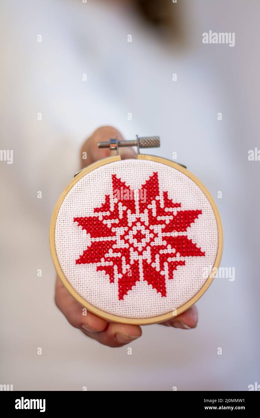 Woman holding hand made cross stitch folk Christmas decoration ornament embroidery on plywood. Nordic snowflakes. Stock Photo