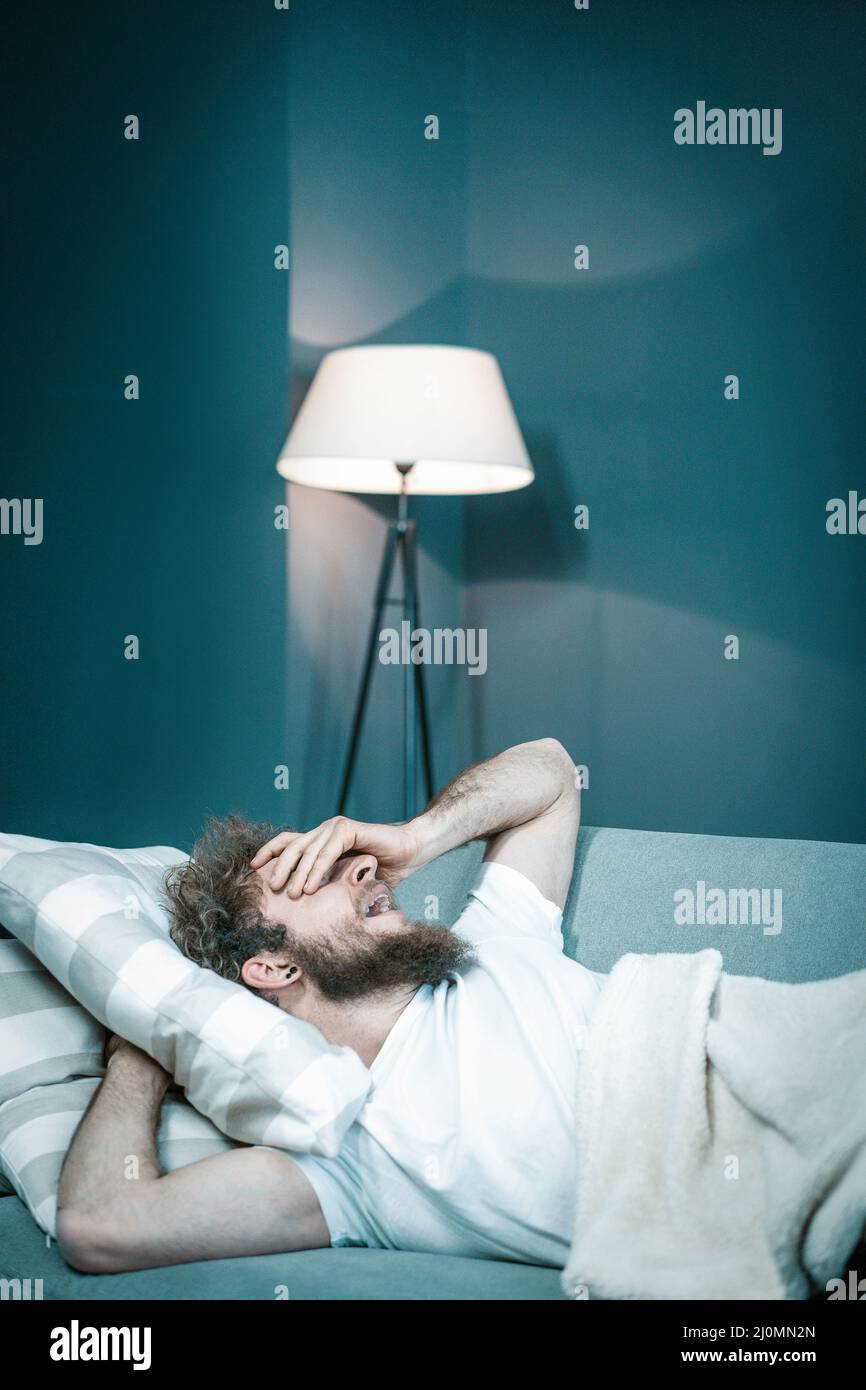 Caucasian Guy Wants to Sleep But Cannot Because of Noisy Neighbors. Tired Man Lies in His Bed and Yawns. Close-up. Bedroom Backg Stock Photo