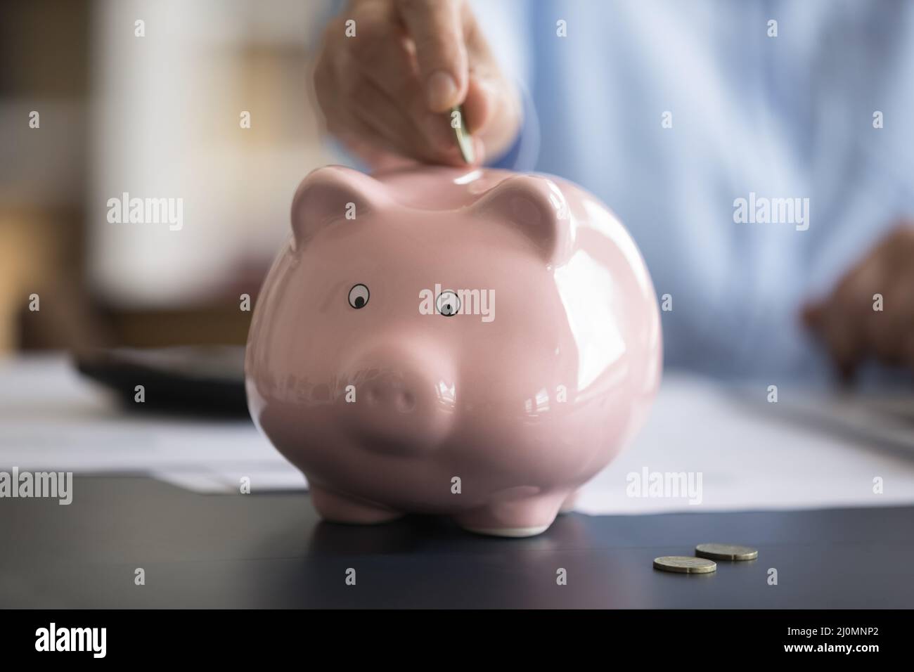 Close up cropped image female hand putting coin in piggybank Stock Photo