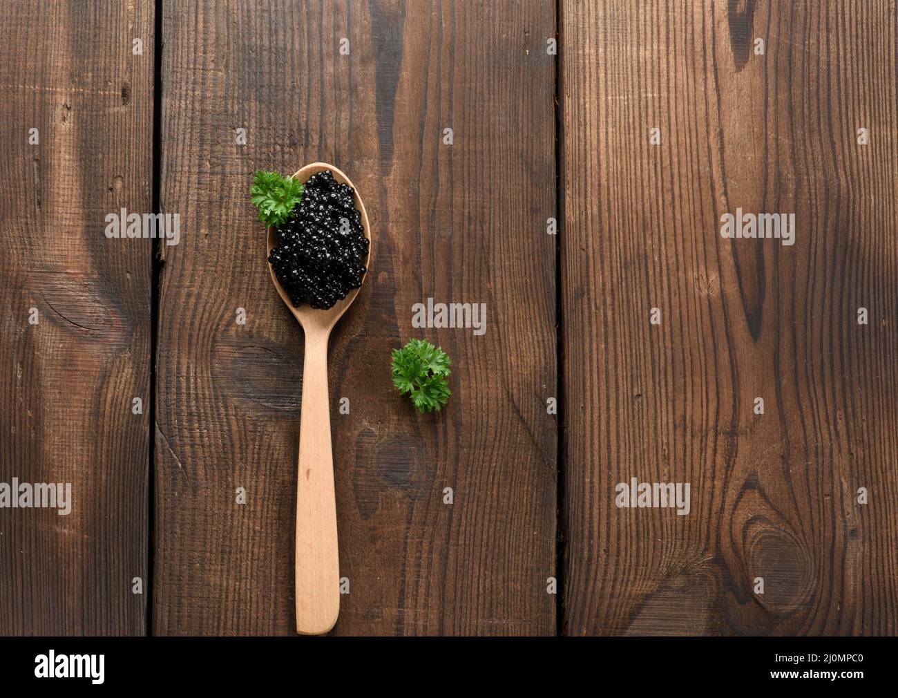 Fresh grainy black paddlefish caviar in brown wooden spoon on a black background, top view Stock Photo