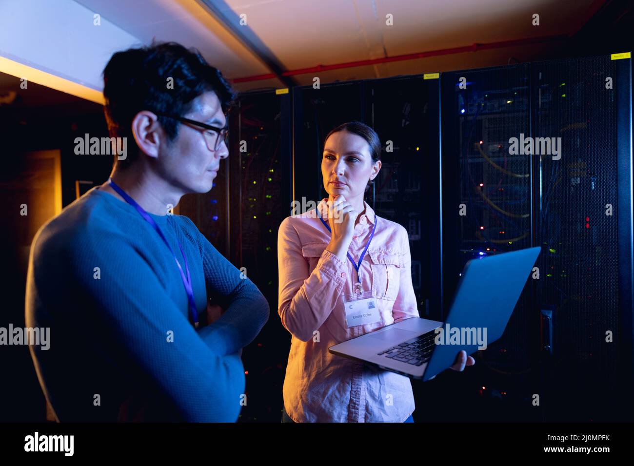 Diverse male and female engineers using laptop in computer server room ...