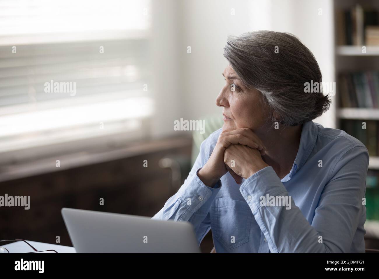 Serious pensive older businesswoman distracted from work staring out window Stock Photo