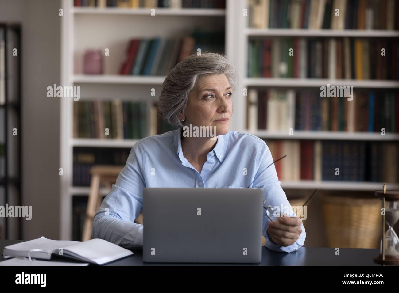 Older businesswoman sit at workplace distracted from work staring aside Stock Photo