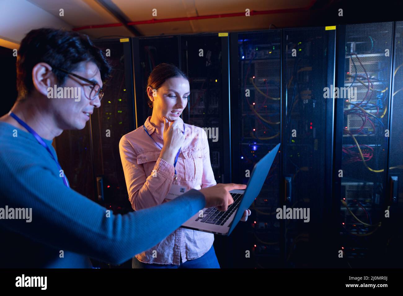Diverse male and female engineers using laptop in computer server room ...