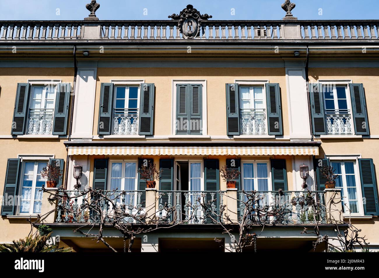 Metal balcony on the facade of the building with shutters on the windows. Como, Italy Stock Photo