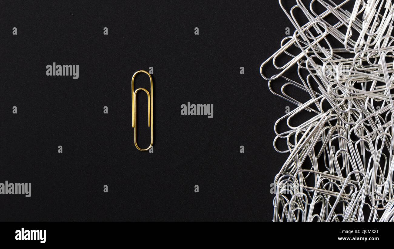 Bright golden paperclip standing out from silver clips black background
