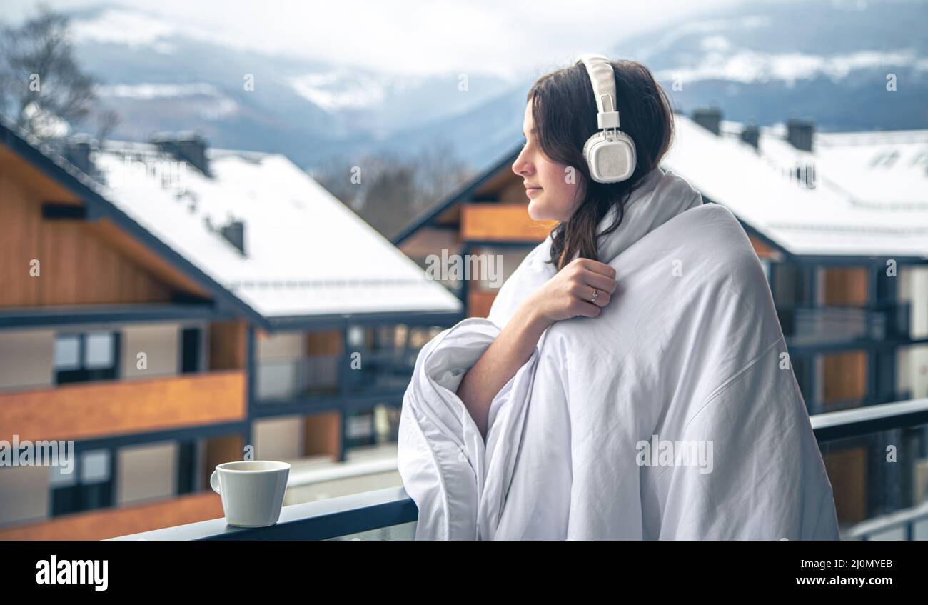 A young woman is listening to music wrapped in a blanket on the balcony ...