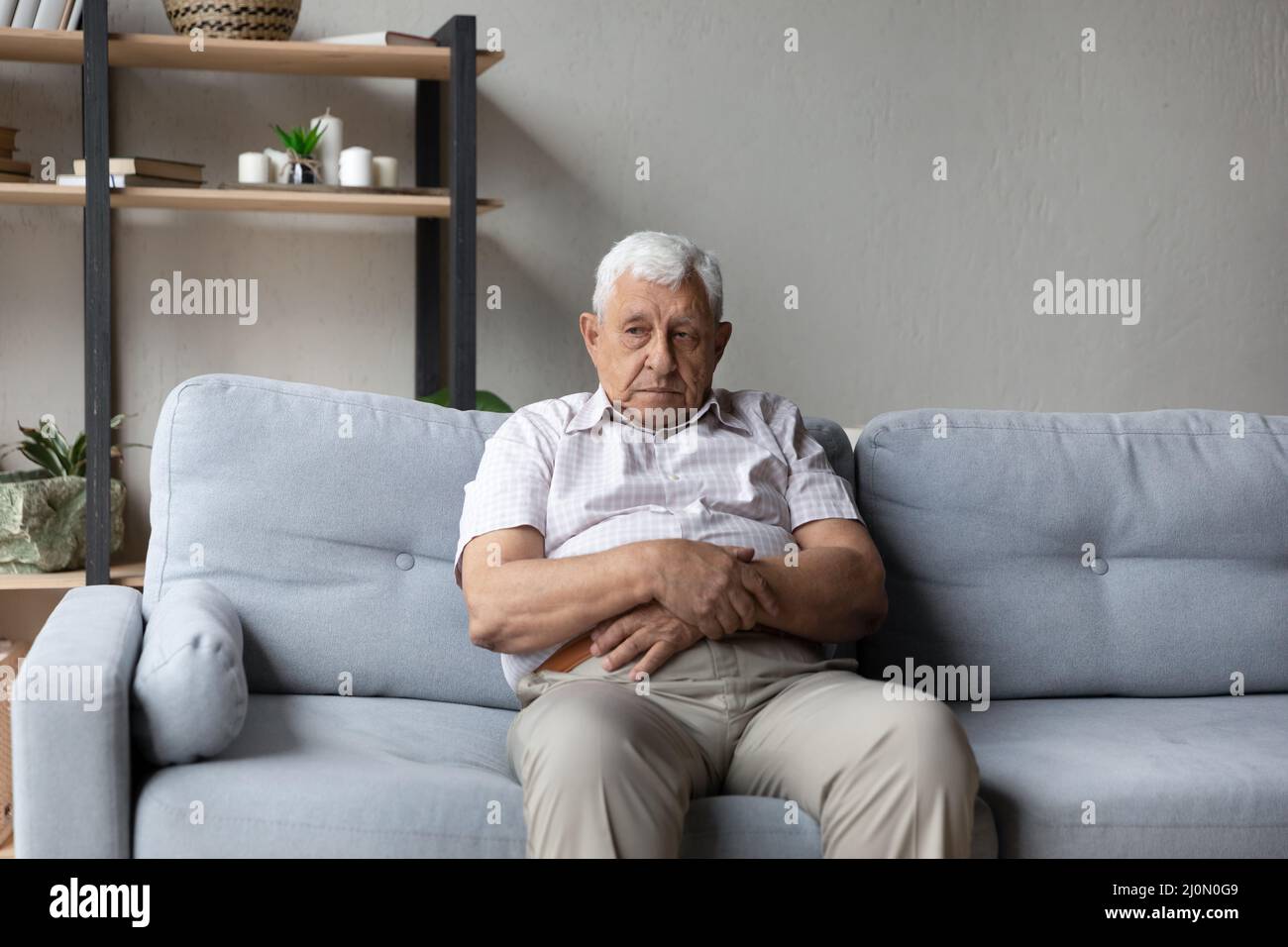 Thoughtful older man sits alone on sofa lost in thoughts Stock Photo