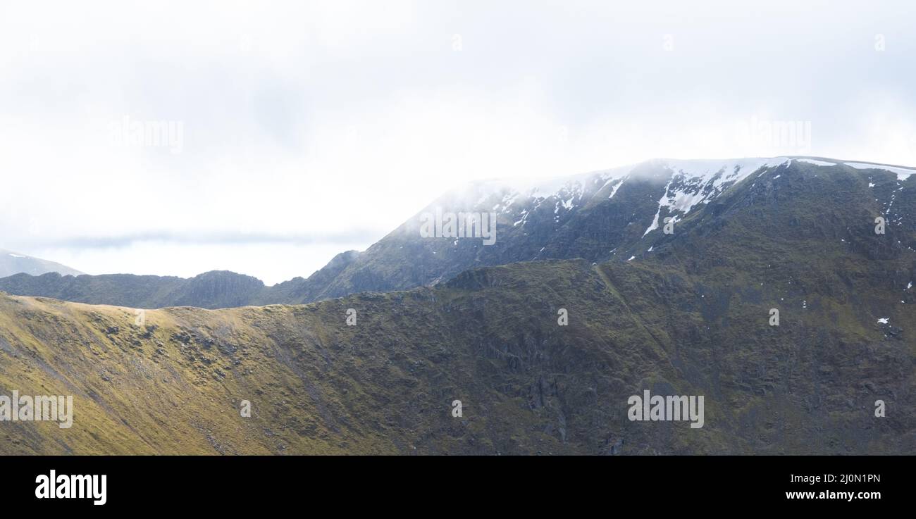 The snow capped peak of Helvellyn in the Lake District, with Swirral Edge and Striding edge visible in the backround, UK Stock Photo