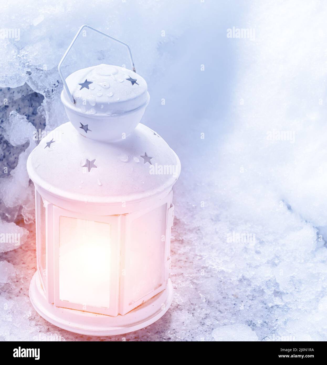 Christmas white lantern. Shines warm light against the background of white snow. Illuminates the road to the holiday Stock Photo