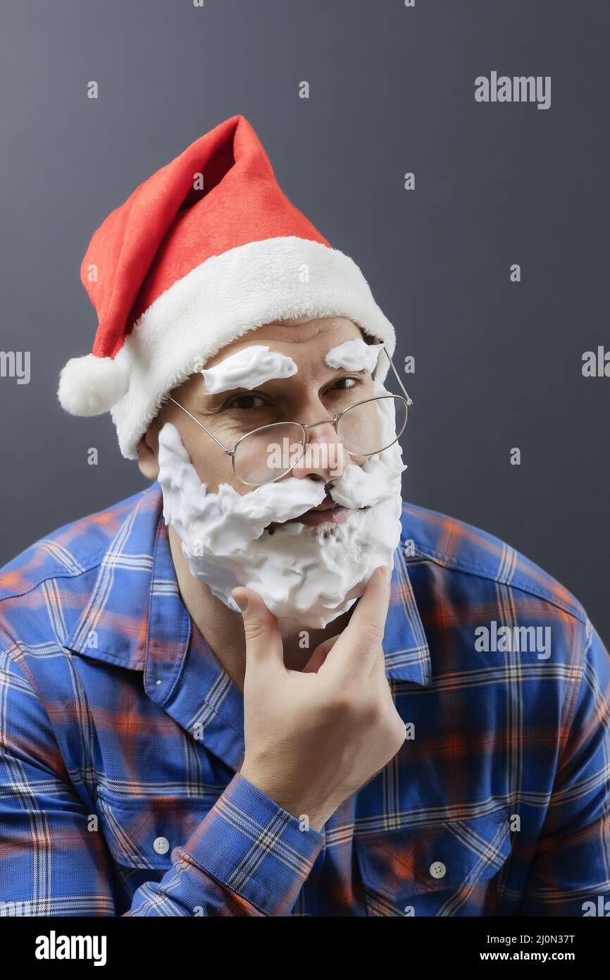 A dressed-up santa with a white foam beard squinting and holding his chin with his fingers. Fake santa. Christmas poster Stock Photo