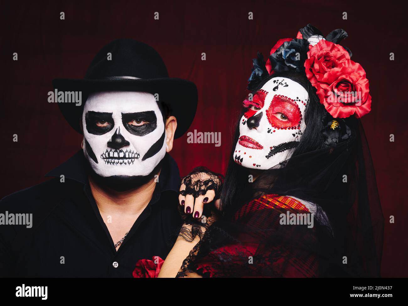 Beautiful woman with a sugar skull makeup with a wreath of flowers on her head and a skeleton man in a black hat Stock Photo