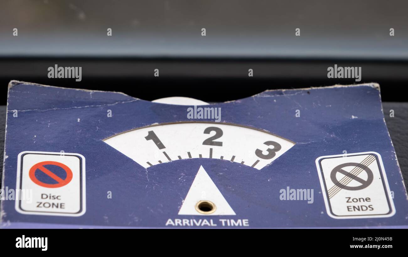 Close up of a blue parking disk beside a windshield indicating arrival time Stock Photo