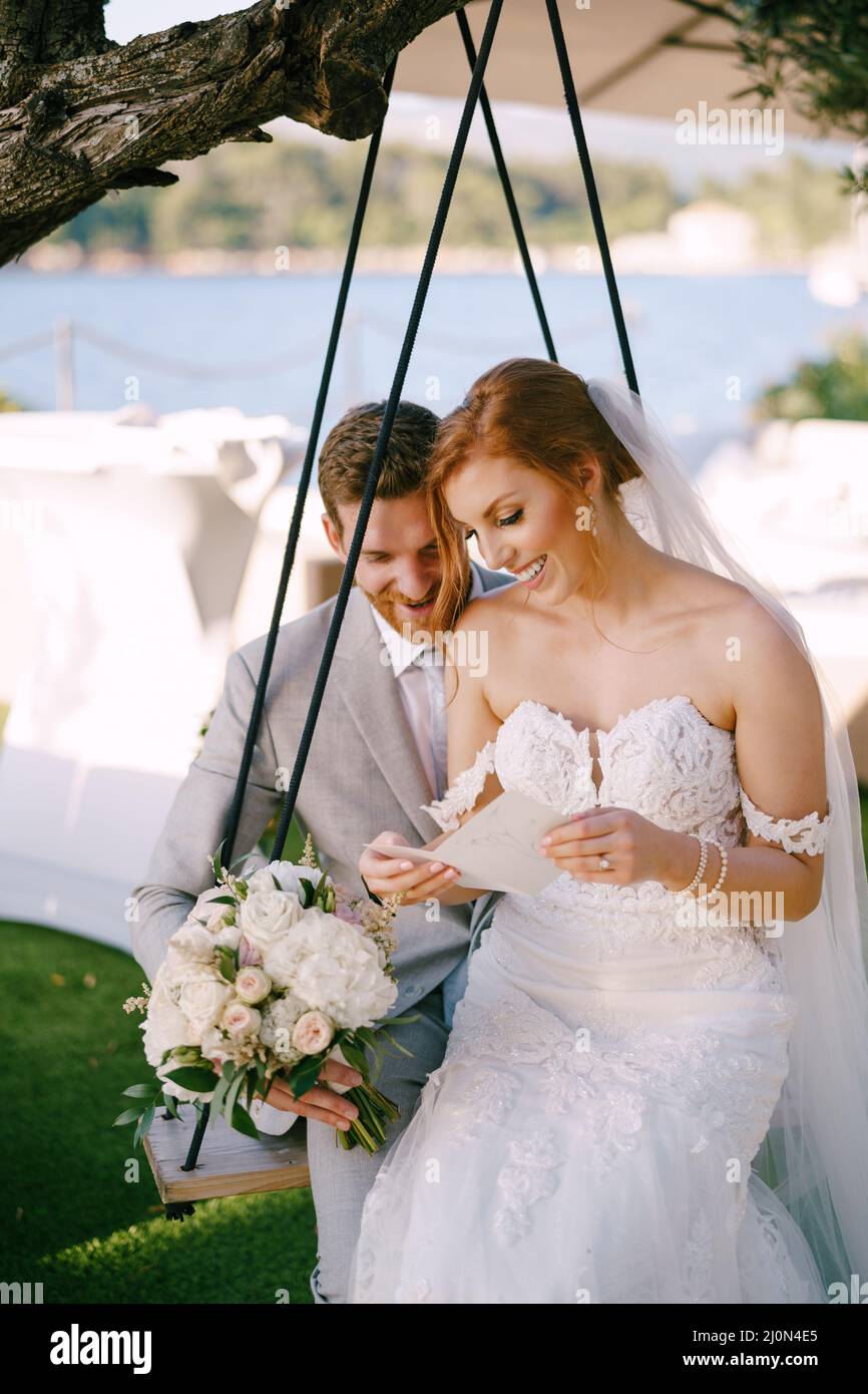 Bride and groom sit on a swing and read a postcard Stock Photo