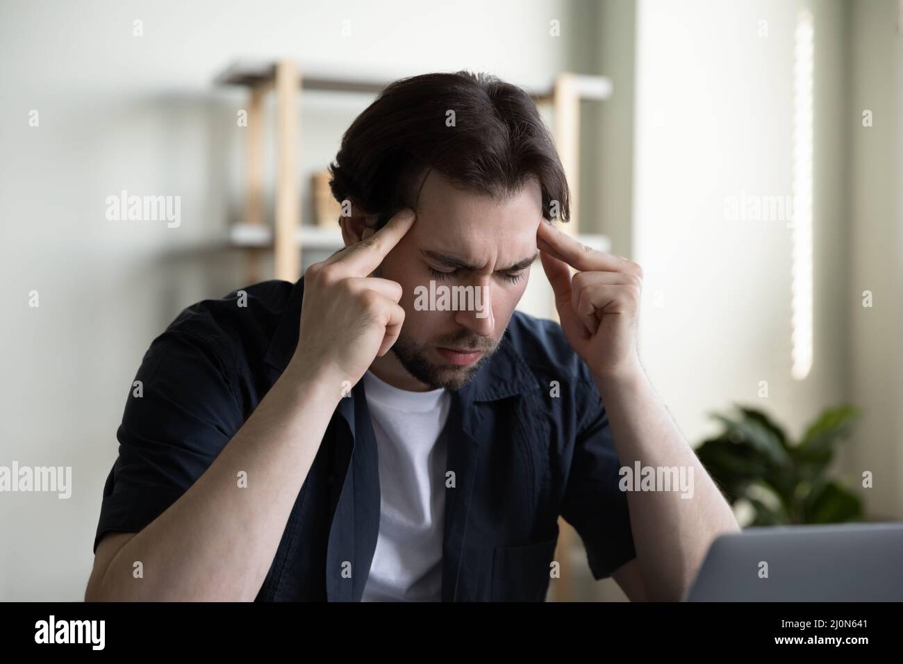 Stressed focused millennial businessman with closed eyes touching head Stock Photo