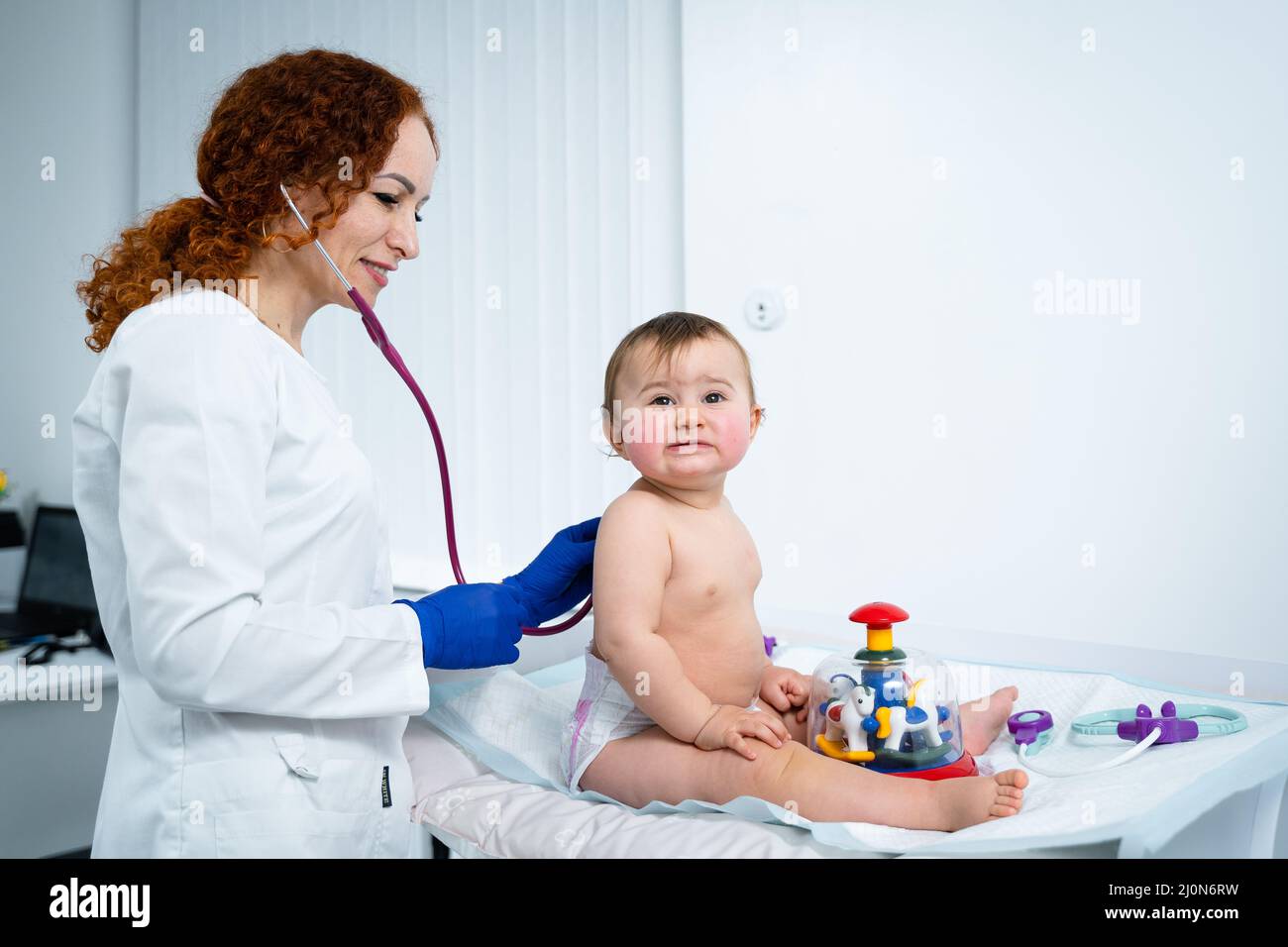 Pediatrician doctor concept. Children medical care. One year old baby girl examined by female pediatrician in clinic office. Chi Stock Photo