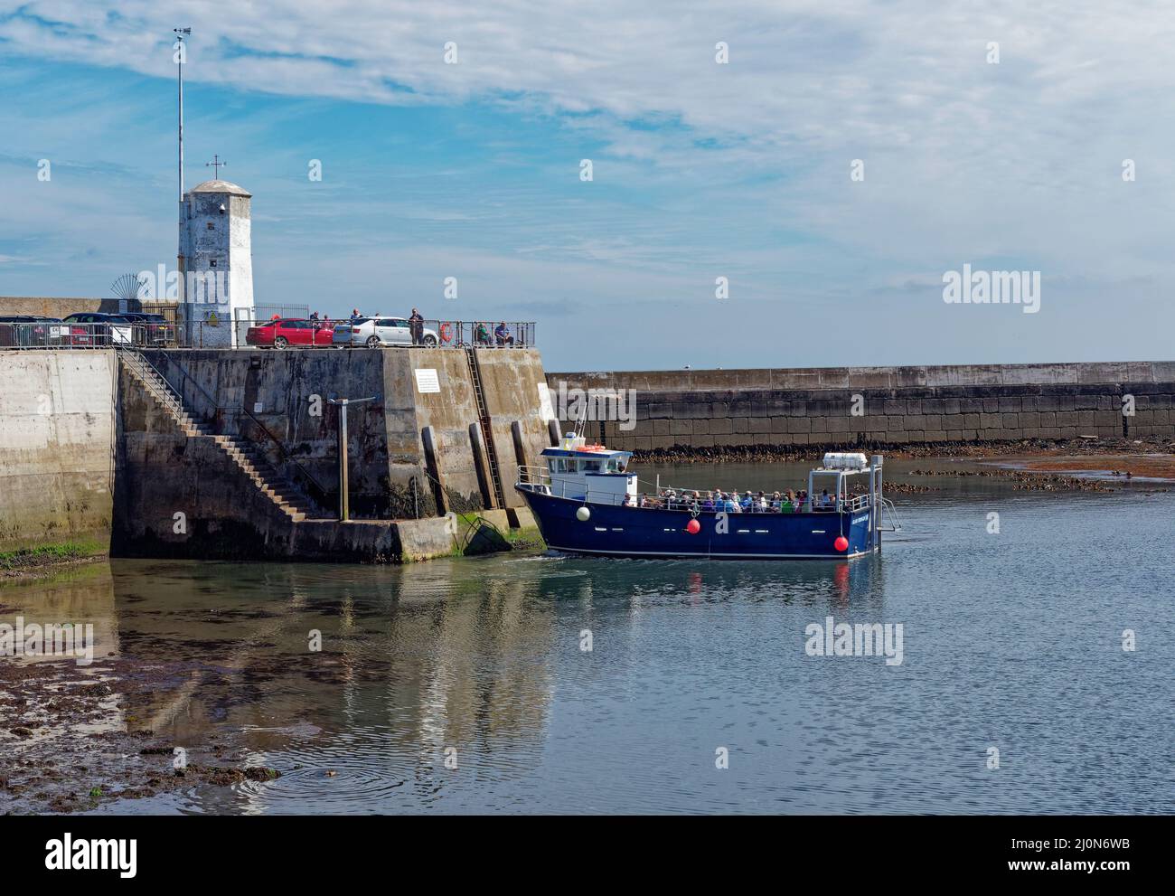 A Blue Hulled  pleasure Craft taking People on Trips to the Farne Islands coming alongside Seahouses Harbour Walls at Low Tide. Stock Photo