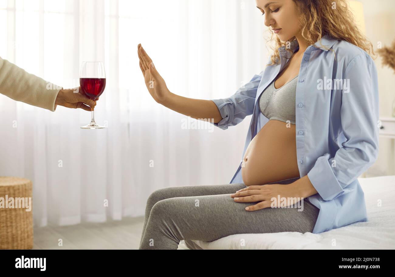 Pregnant woman shows stop gesture in front of glass of red wine on sign of giving up alcohol. Stock Photo