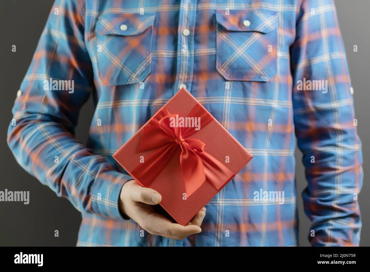 A red gift box with a bow in the hand of a man in a blue plaid shirt. Festive surprise Stock Photo