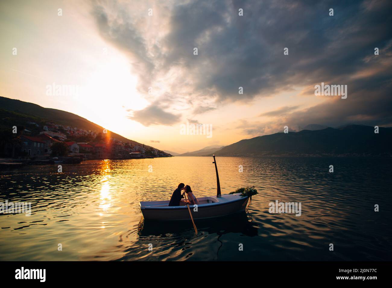 Man and woman kiss in a boat in the middle of the water against the backdrop of the sunset Stock Photo
