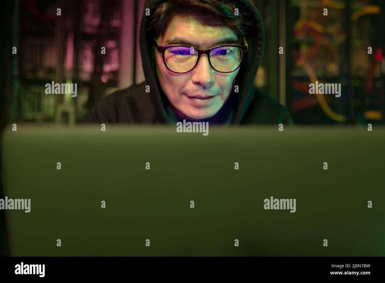 Asian male hacker using a laptop in computer server room Stock Photo