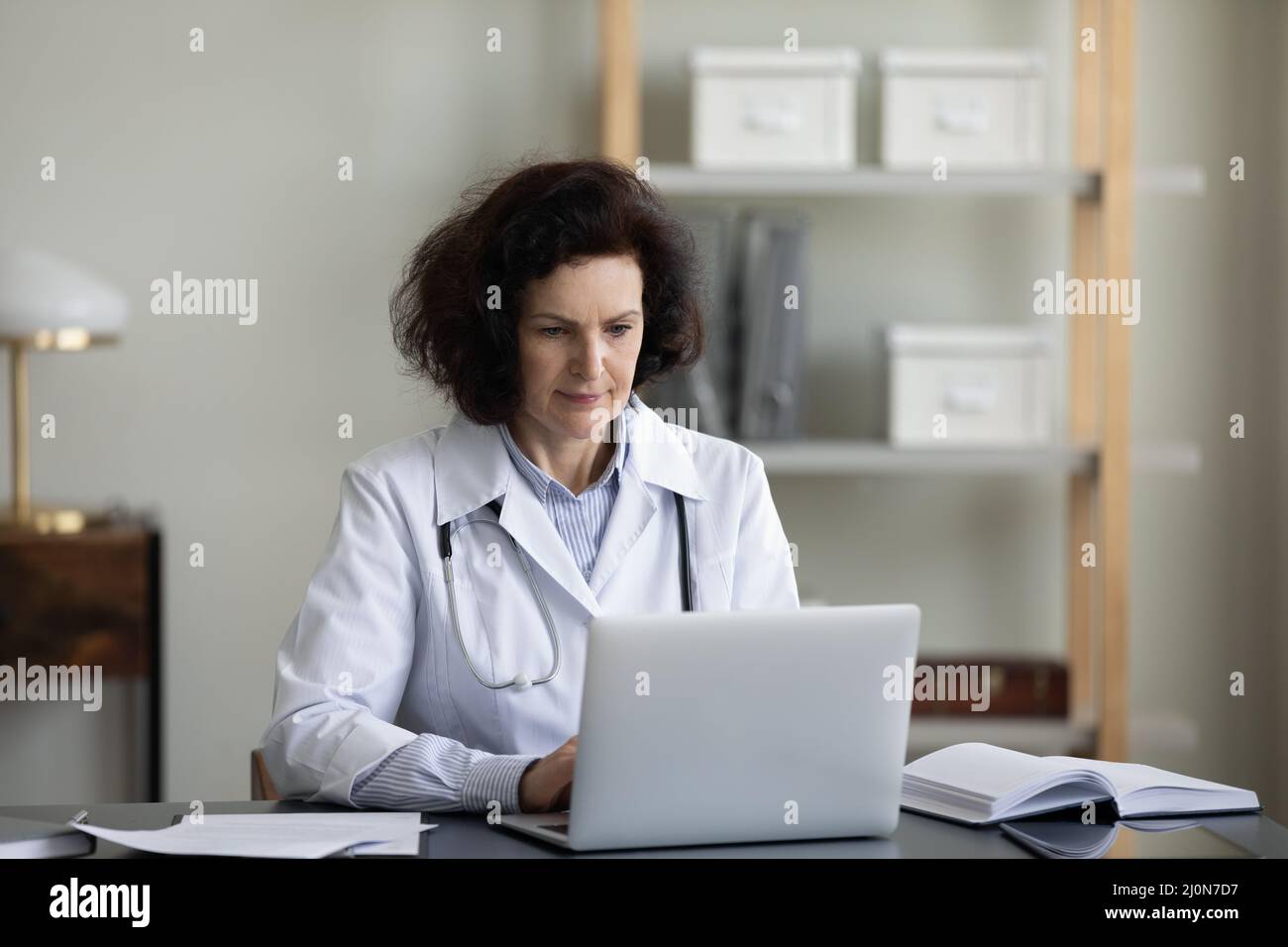 Serious senior chief doctor woman using laptop at workplace Stock Photo
