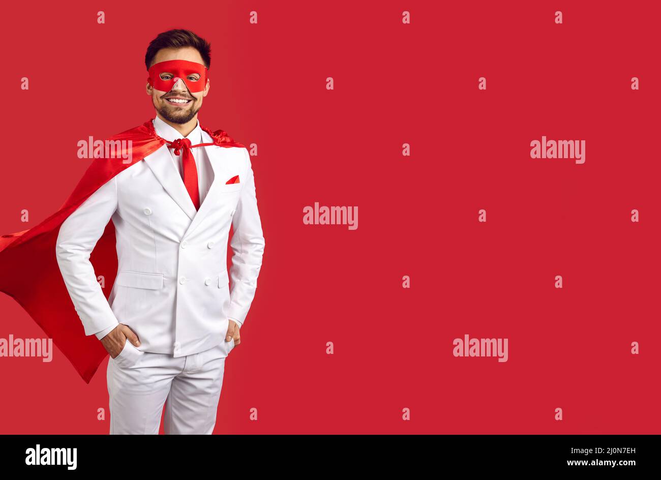 Happy handsome superman in suit, mask and cape standing on red copy space background Stock Photo