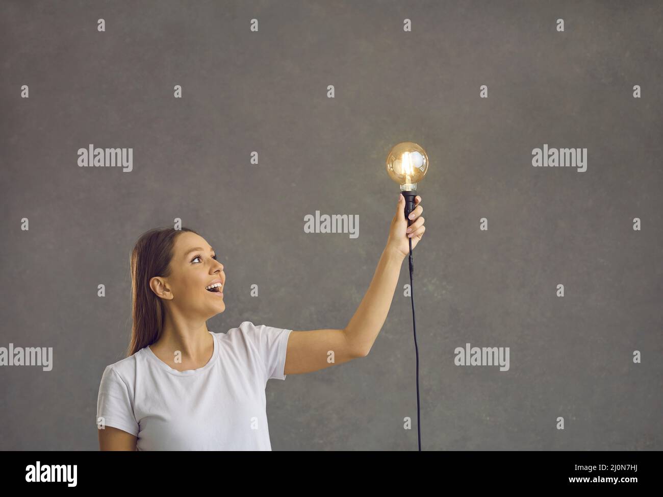 Charming smiling cute young woman holding a light bulb in her left hand smiling and looking at her. Stock Photo
