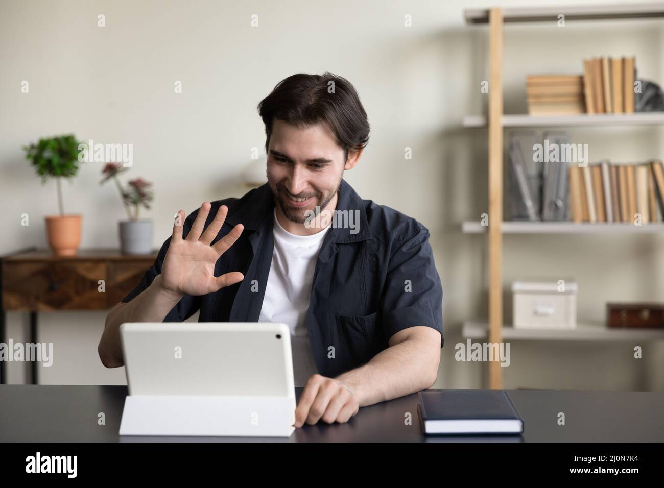 Happy friendly freelance guy waving hand hello at gadget screen Stock Photo