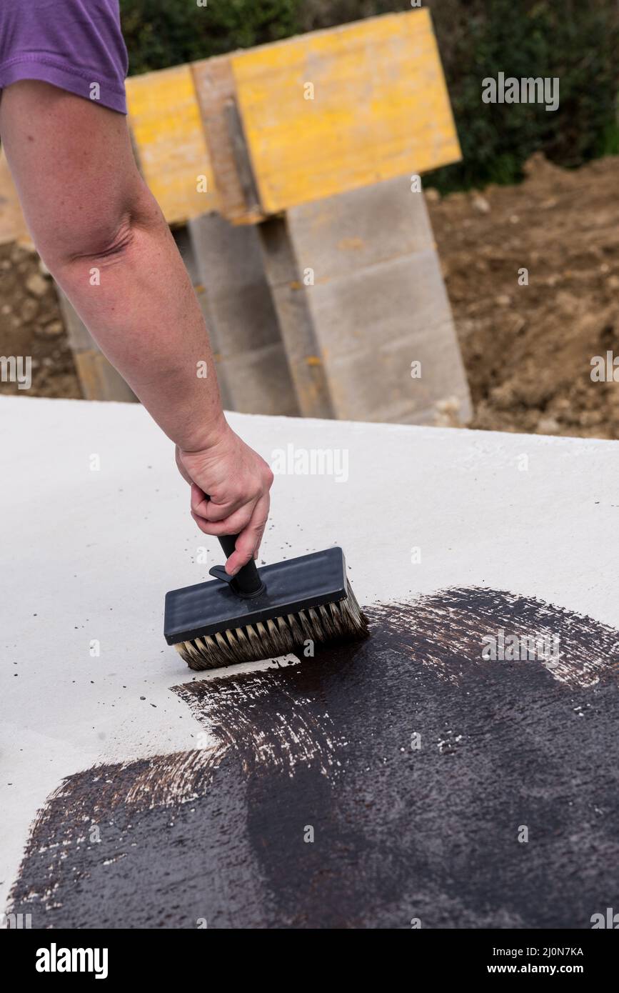 Construction worker paints the basement ceiling on a construction site with bitumen - close-up Stock Photo