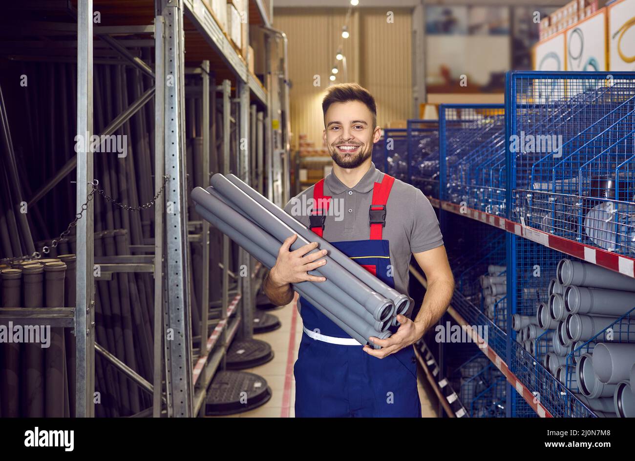 Happy young salesman standing in one of the store aisles and holding PVC drain pipes Stock Photo