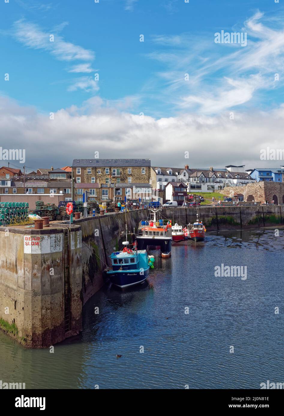 Seahouses  Harbour at Low Tide, with Boats resting on the silty bottom of the Harbour, overlooked by Houses and Commercial Buildings. Stock Photo