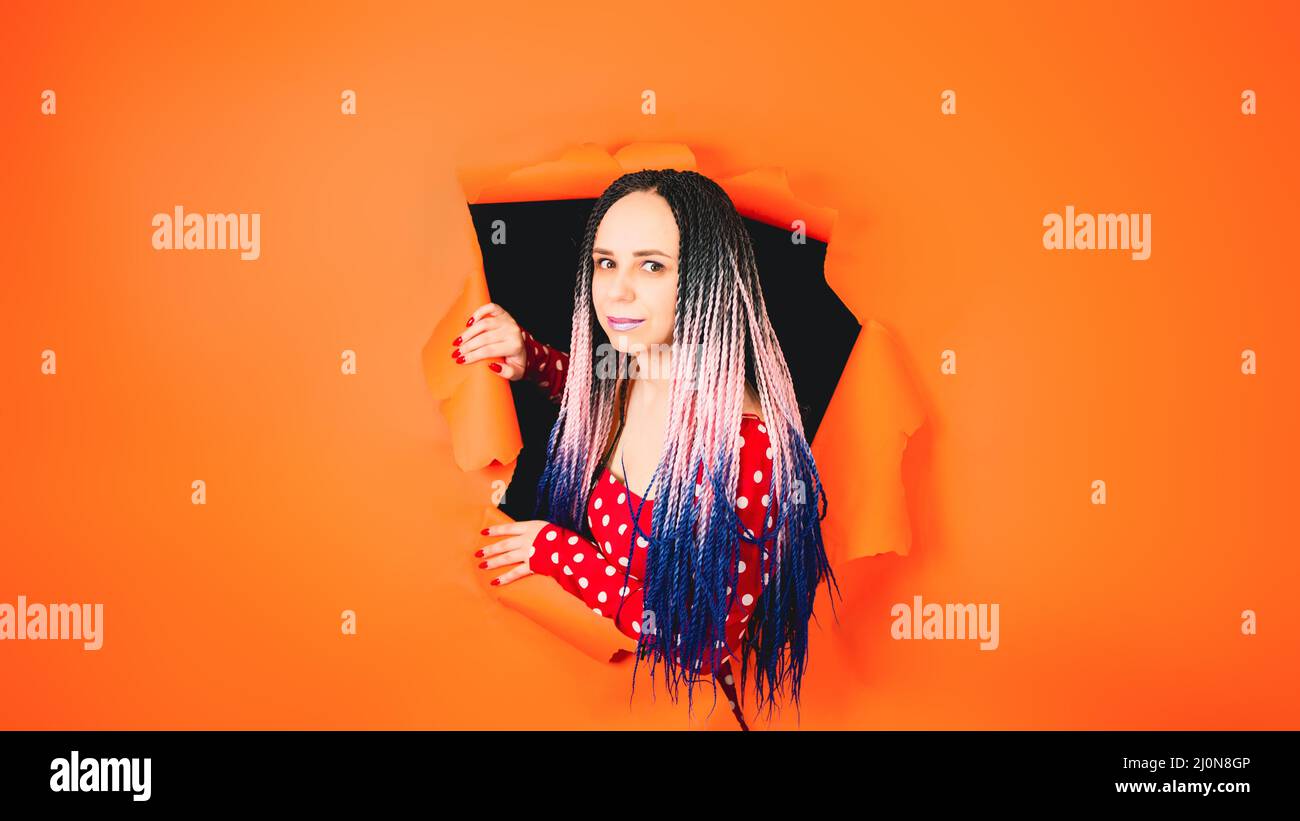 A stylish girl in a bright red dress looks at the camera through a hole ...