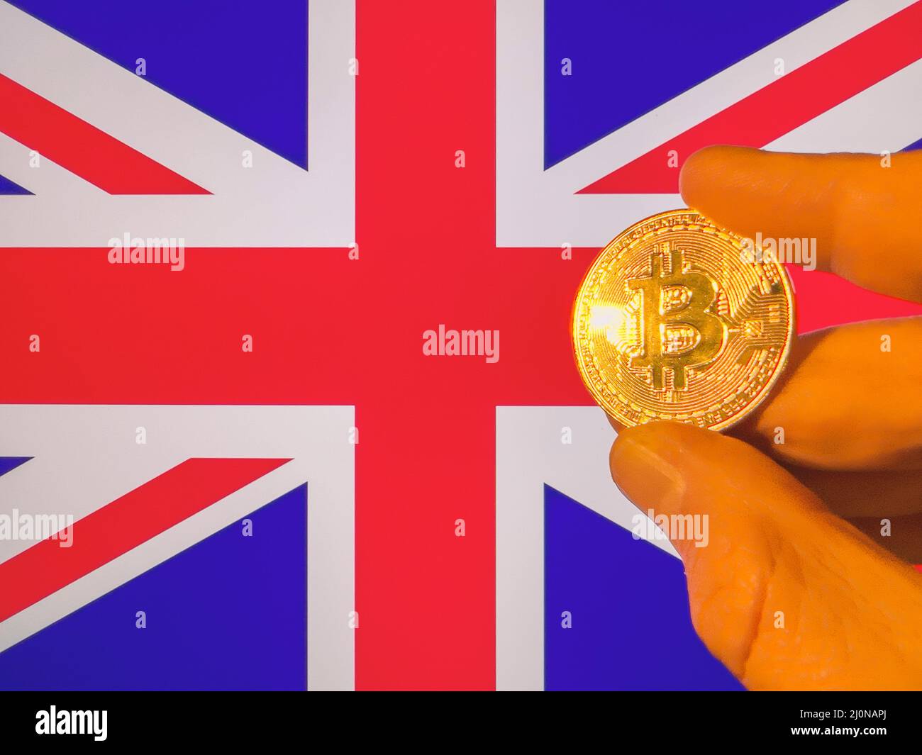 Holding a physical golden Bitcoin over the British flag. England as cryptocurrency and blockchain technology investor. Financial background Stock Photo
