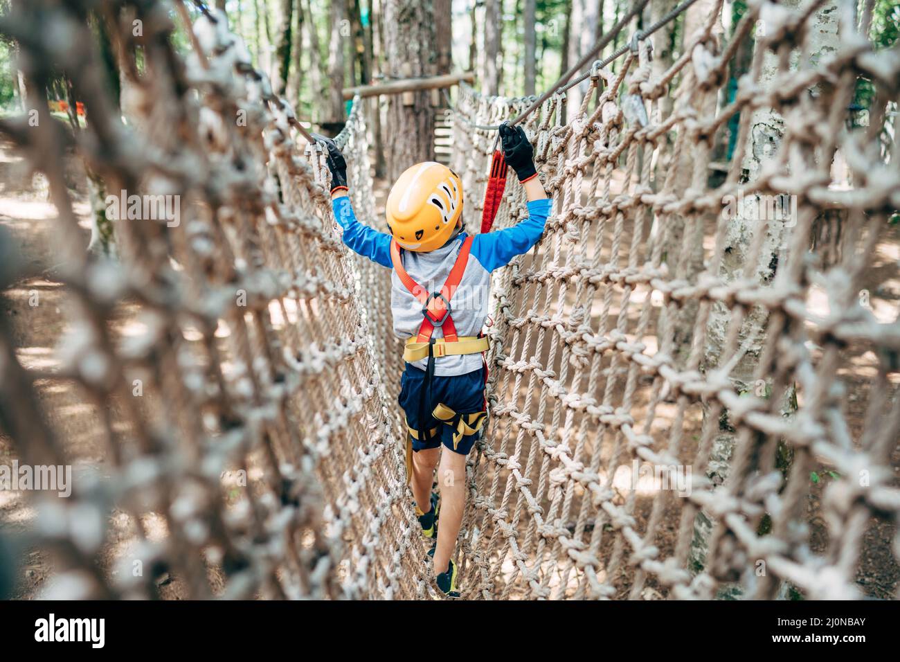 Boy walks across a mesh bridge, holding onto a cable. Back view Stock Photo